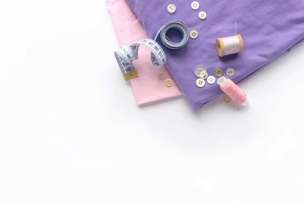 Sewing accessories and fabric on a white background. Fabric, sewing threads, needle, buttons and sewing centimeter. top view, flatlay