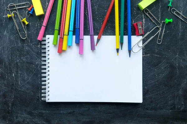 School supplies and notebook on a chalkboard background. Free space for text — Stockfoto