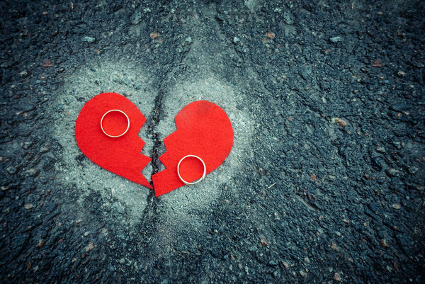 Divorce concept - broken heart with wedding rings on cracked asphalt. Toned