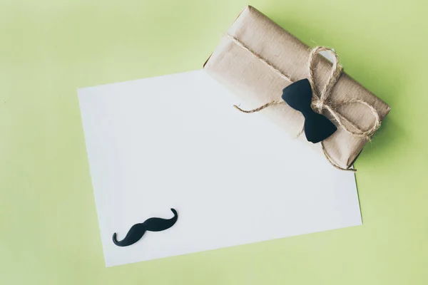 Alla festa del papà. Pacchetto regalo avvolto con carta e corda con papillon decorativo su sfondo verde. Copyspace — Foto Stock