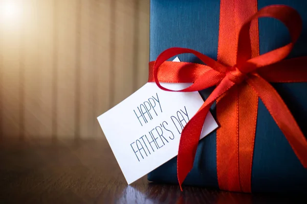 Fathers day. Gift package wrapped with blue paper and rope with a red ribbon on wooden background