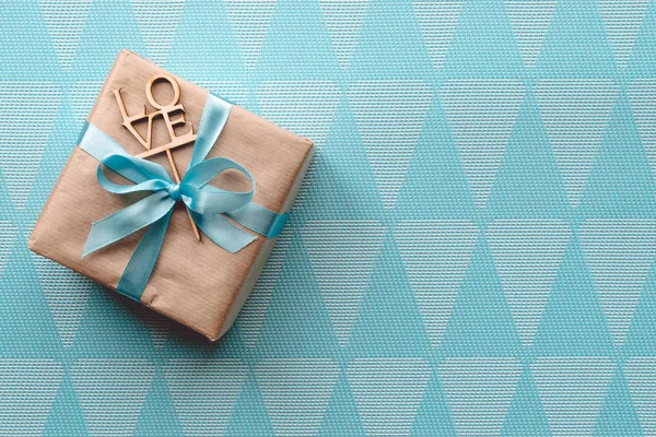 Scatola regalo avvolta in carta marrone con nastro azzurro su sfondo blu. Freespace — Foto Stock