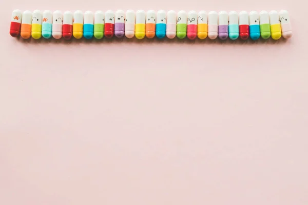 Fila de cápsula em um papel pastel fundo rosa. Espaço de cópia. Fronteira de medecinas multicoloridas engraçadas — Fotografia de Stock