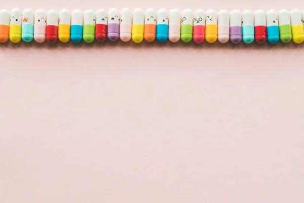Fila de cápsula sobre un fondo de papel pastel rosa. Copyspace. Frontera de medicinas de colores divertidos — Foto de Stock