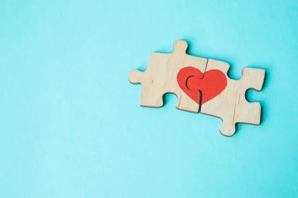 Red heart is drawn on the pieces of the wooden puzzle lying next to each other on blue background. Love concept. St. Valentine day. Copy space. — Stock Photo, Image