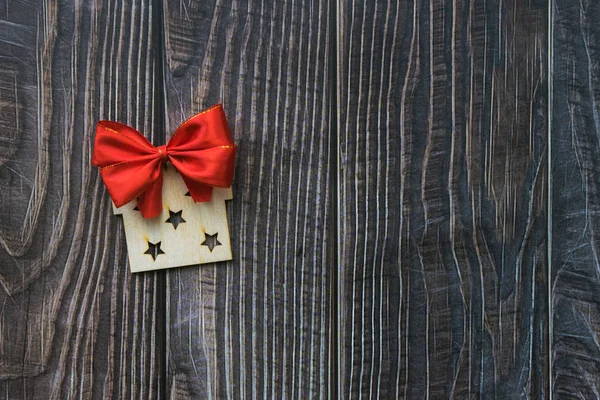 Świąteczne tło z drewnianym ozdobnym prezentem i czerwoną kokardą na starej drewnianej płycie — Zdjęcie stockowe