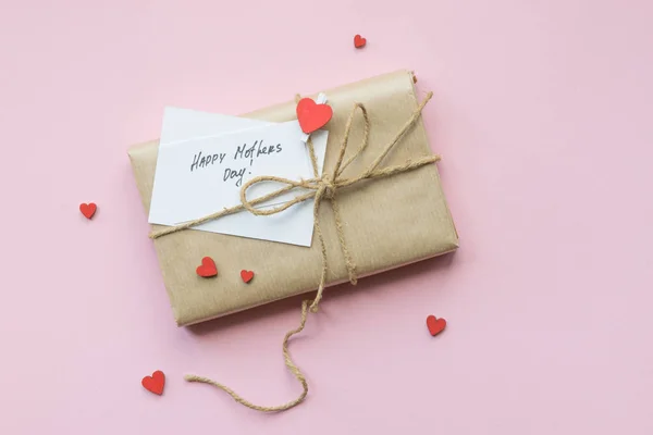 Geschenk in braunes Bastelpapier gewickelt und Hanfband auf hellrosa Hintergrund gebunden. Geschenkbox mit Grüßen zum Muttertag. Ansicht von oben. — Stockfoto