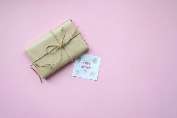 Presenteert verpakt in bruin ambachtelijk papier en bindtouw op lichtroze achtergrond. Geschenkdoos met groeten op Moederdag. Bovenaanzicht. — Stockfoto