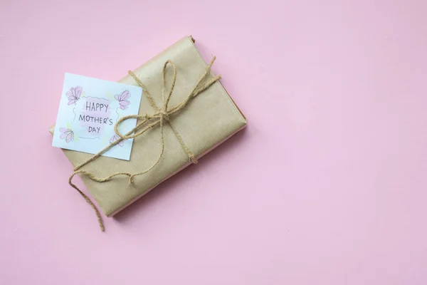 Presenta avvolto in carta artigianale marrone e stringa di canapa cravatta su sfondo rosa chiaro. Confezione regalo con auguri per la Festa della Mamma. Vista dall'alto . — Foto Stock