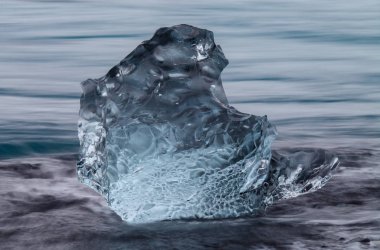 Diamond beach Jokulsarlon lagoon, İzlanda yakınındaki siyah kum ile şaşırtıcı şeffaf mavi buzdağı parçalar. Yavrulama buz. Su uzun pozlama.