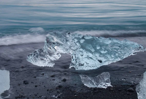 Geweldig transparante blauwe ijsberg stukken op Diamond strand met zwart zand in de buurt van Jokulsarlon lagoon, IJsland. Ijs kalven. Water lange blootstelling. — Stockfoto