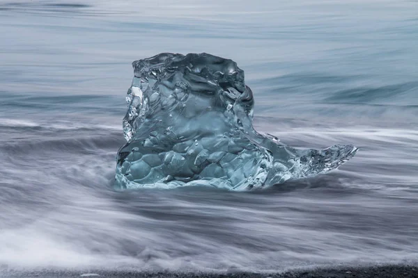 Geweldig transparante blauwe ijsberg stukken op Diamond strand met zwart zand in de buurt van Jokulsarlon lagoon, IJsland. Ijs kalven. Water lange blootstelling. — Stockfoto