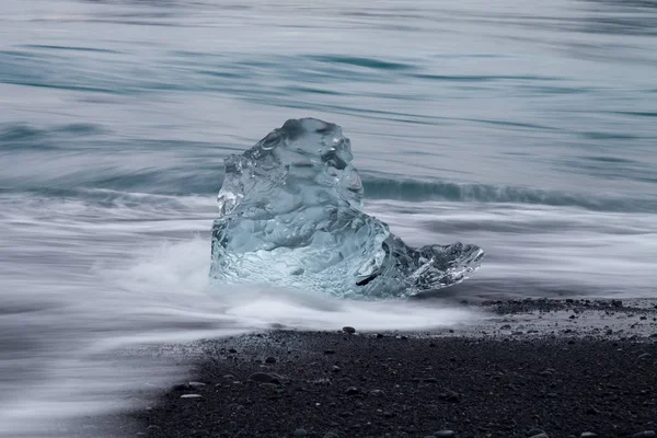Csodálatos darab átlátszó kék jéghegy Diamond beach, a fekete homokos közelében Jokulsarlon lagúna, Izland. Ice ellés. Víz hosszú expozíció. — Stock Fotó