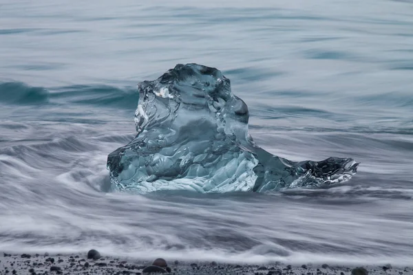 Geweldig transparante blauwe ijsberg stukken op Diamond strand met zwart zand in de buurt van Jokulsarlon lagoon, IJsland. Ijs kalven. Water lange blootstelling. — Stockfoto