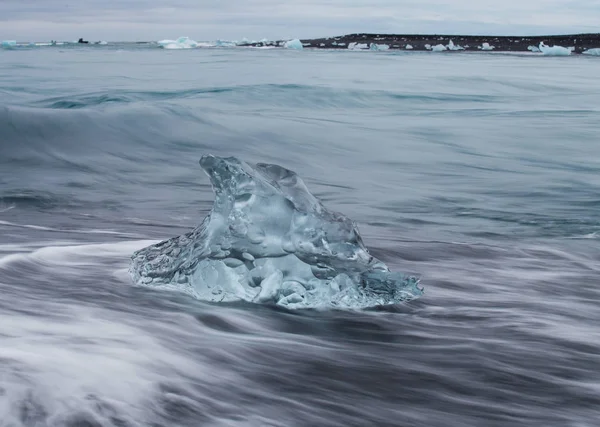 驚くほど透明な青い氷山作品ダイヤモンド手配ラグーン、アイスランド付近の黒砂のビーチ。氷の分娩します。水の長時間露光. — ストック写真