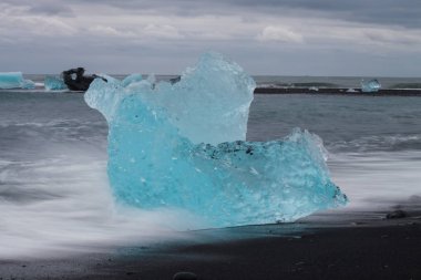 Diamond beach Jokulsarlon lagoon, İzlanda yakınındaki siyah kum ile şaşırtıcı şeffaf mavi buzdağı parçalar. Yavrulama buz. Su uzun pozlama.