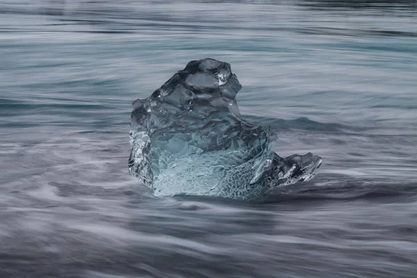 Amazing transparent blue iceberg pieces on Diamond beach with black sand near Jokulsarlon lagoon, Iceland. Ice calving. Water long exposure. — Stock Photo, Image