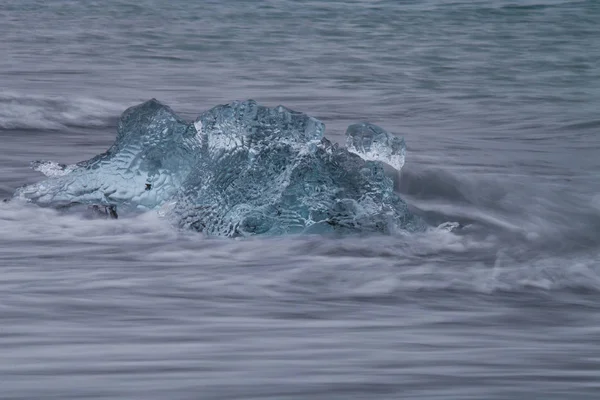 Amazing transparent blue iceberg pieces on Diamond beach with black sand near Jokulsarlon lagoon, Iceland. Ice calving. Water long exposure. — Stock Photo, Image