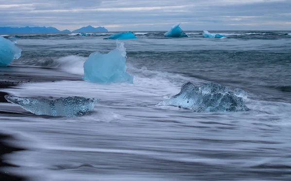 Superbe iceberg bleu transparent sur la plage de Diamond avec du sable noir près de la lagune de Jokulsarlon, en Islande. Vêlage sur glace. Eau longue exposition . — Photo
