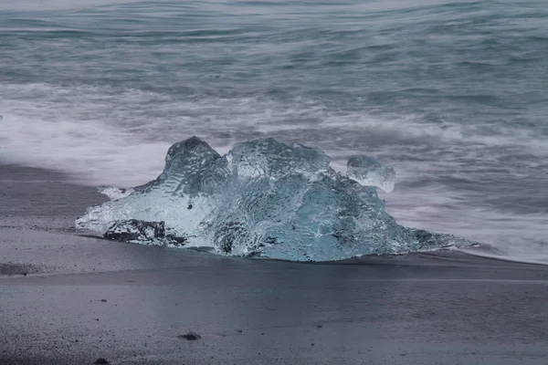 Niesamowite kawałki przezroczysty niebieski góry lodowej na diament plaży z czarnym piaskiem, w pobliżu laguny Jokulsarlon, Islandia. Cielenie się. Długi czas ekspozycji wody. — Zdjęcie stockowe