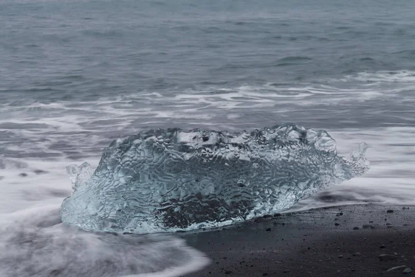 Csodálatos darab átlátszó kék jéghegy Diamond beach, a fekete homokos közelében Jokulsarlon lagúna, Izland. Ice ellés. Víz hosszú expozíció. — Stock Fotó