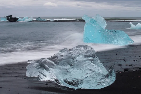 Amazing transparent blue iceberg pieces on Diamond beach with black sand near Jokulsarlon lagoon, Iceland. Ice calving. Water long exposure. — Stock Photo, Image