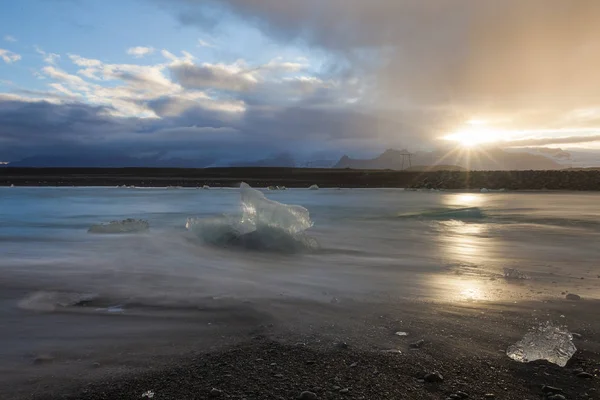 Dramático atardecer con increíbles piezas de iceberg azul transparente en la playa Diamond con arena negra cerca de la laguna de Jokulsarlon, Islandia. Terneros de hielo. Agua larga exposición . — Foto de Stock