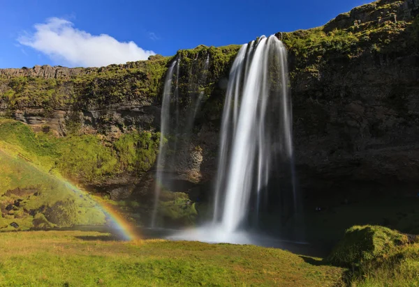 Maravillosa vista de la cascada Seljalandsfoss en Islandia. Día de sol en verano con arco iris y paisaje verde. Monumento famoso en la ruta número uno . — Foto de Stock
