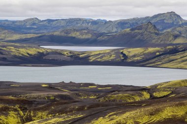 Yeşil bir tepe ve siyah lav ve mavi ayna dağ gölü ile dramatik İzlanda manzara. İzlanda
