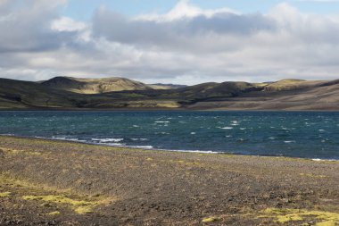 Yeşil bir tepe ve siyah lav ve mavi ayna dağ gölü ile dramatik İzlanda manzara. İzlanda