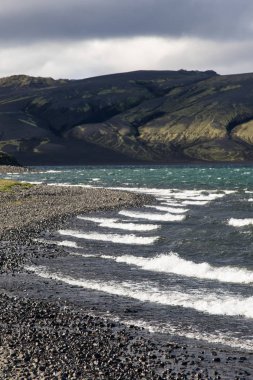 Yeşil bir tepe ve siyah lav ve mavi ayna dağ gölü ile dramatik İzlanda manzara. İzlanda