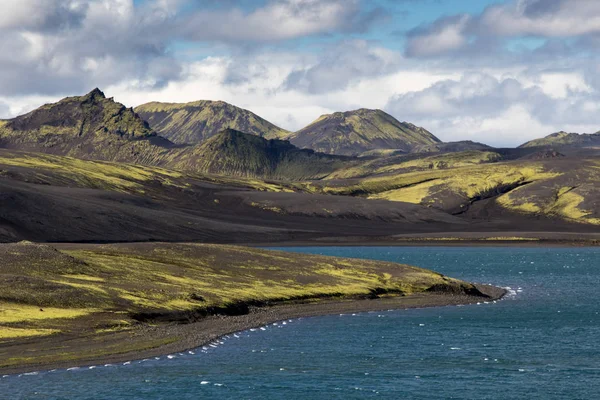 Dramático paisaje de iceland con una colina verde y lava negra y un espejo azul lago de montaña. Islandia — Foto de Stock