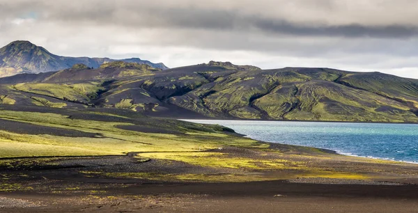 Dramático paisaje de iceland con una colina verde y lava negra y un espejo azul lago de montaña. Islandia — Foto de Stock
