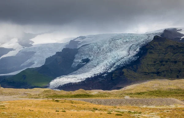 Langue du glacier en Islande dérivant de la montagne de mousse verte dans la journée brumeuse. La glace bleue du glacier est visible, ainsi que la mousse verte recouvrant les rochers de la montagne — Photo