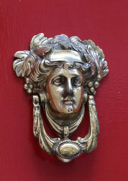 Decorative bronze traditional malttese door handle in the form of a beautiful womans head on a red painted door. Malta