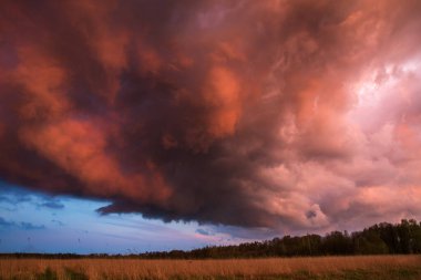 Fırtınadan önce gün batımında kabarık bulutlu görkemli, renkli, dramatik kırmızı gökyüzü ve geniş tarlalı yağmur manzarası..