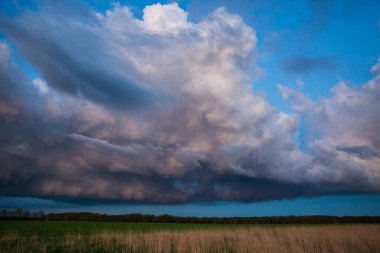 Fırtınadan önce gün batımında kabarık bulutlu görkemli, renkli, dramatik kırmızı gökyüzü ve geniş tarlalı yağmur manzarası..