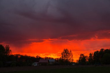 Fırtınadan önce gün batımında kabarık bulutlu görkemli, renkli, dramatik kırmızı gökyüzü ve geniş tarlalı yağmur manzarası..