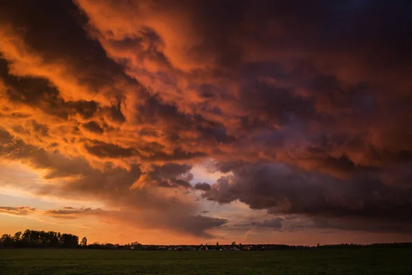 Landscape with majestic colorful dramatic red sky with fluffy clouds at sunset before before a thunderstorm and rain with the spacious field.