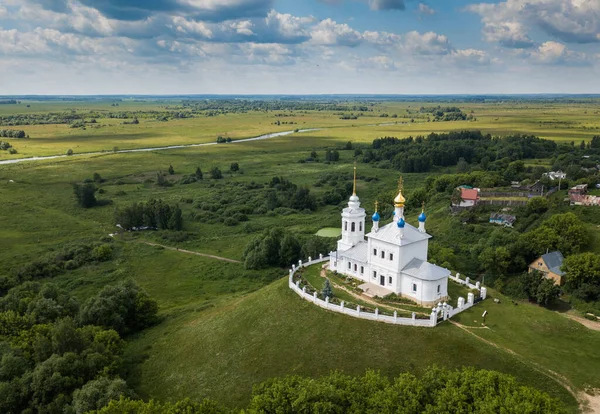 Vista aérea do verão da igreja solitária branca que está em uma colina entre campos verdes e rio. Rússia — Fotografia de Stock