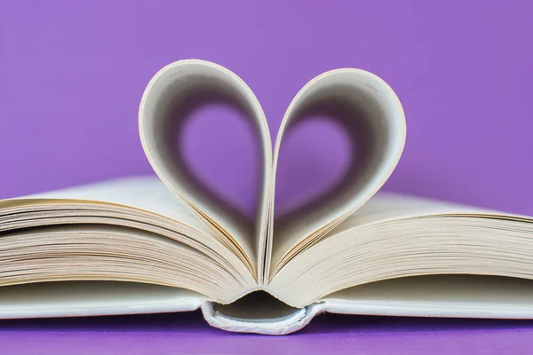 White book with pages that form a heart isolated on purple background. I love reading concept