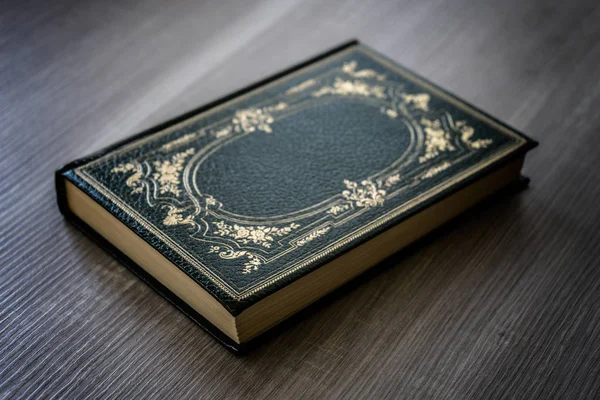 Antyczna książka z zieloną pokrywą ze złotymi dekoracjami spoczywających na drewnianym stole — Zdjęcie stockowe