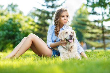Yaz parkında Golden Retriever köpeğiyle çimenlerde oturan genç bir kadın.