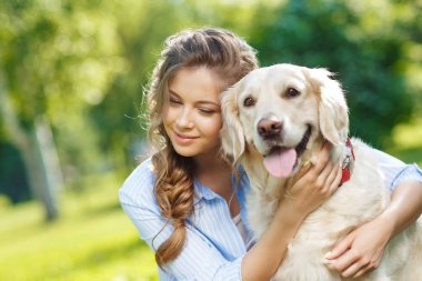 Golden Retriever köpeğiyle yaz parkında genç bir kadın.