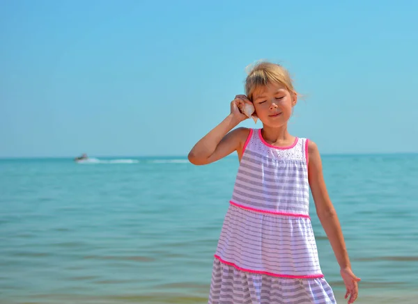 少女は海を背景に貝殻の音を聞く 海での少女の休暇 子供の週末 ストック写真