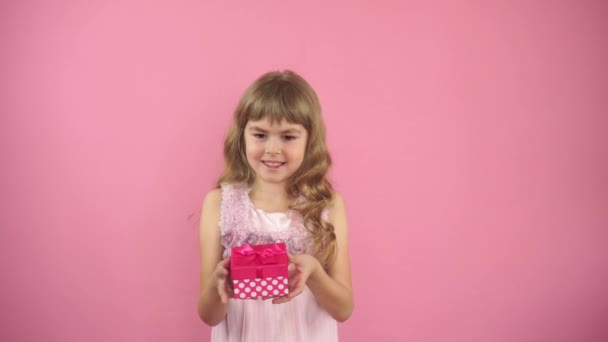 A menina em um fundo rosa examina um presente. A rapariga dá uma caixa com um presente. Presente de aniversário para o bebê. Caixa com um presente nas mãos. Coração fora da caixa. Feliz aniversário. . — Vídeo de Stock