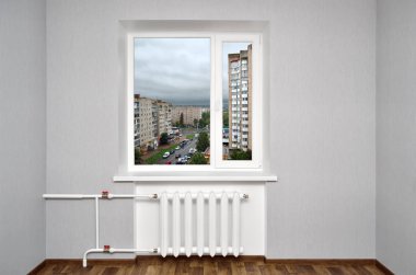 Isıtma ile boş odada beyaz pencere ve gri duvarlar. Cityscape evin penceresinden.