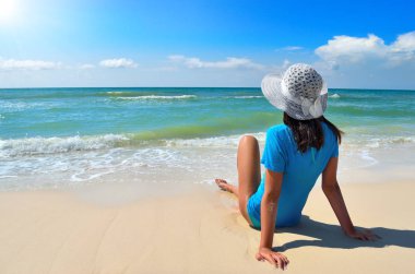 Genç kız deniz sahilde beyaz şapkalı. Mavi deniz karşı temiz, kumlu plaj.