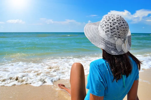 Genç kız deniz sahilde beyaz şapkalı. Mavi deniz karşı temiz, kumlu plaj.