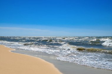 Deniz dalgaları sahili mavi gökyüzüne karşı yıkıyor. Vahşi bir sahilde manzara. Yazın deniz..